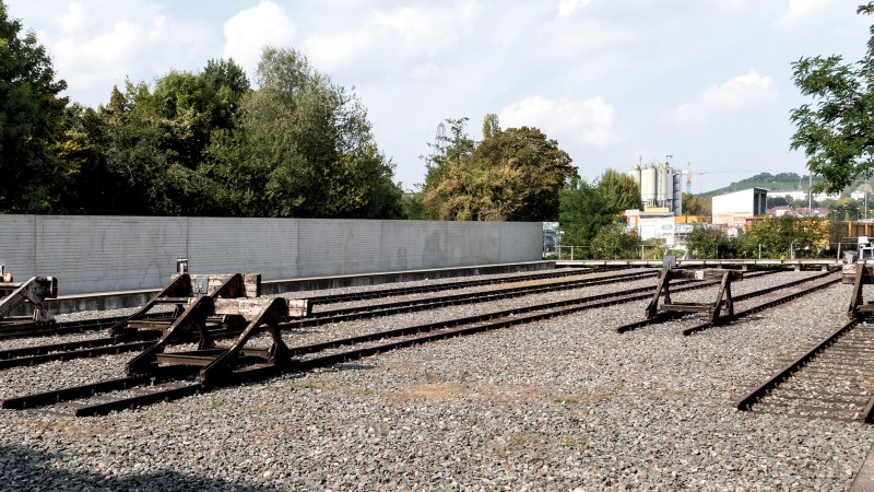 Gedenkst&auml;tte mit stillgelegten Bahngleisen, umgeben von B&auml;umen und einer Mauer. Ein ruhiger Ort des Erinnerns., &copy; Foto-Kunst Andreas Keller