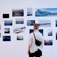 A person looks at a wall with photographs of landscapes and water. The pictures show various natural motifs in cool colors., © OCEAN GALLERY A person looks at a wall with photographs of landscapes and water. The pictures show various natural motifs in cool colors., © OCEAN GALLERY