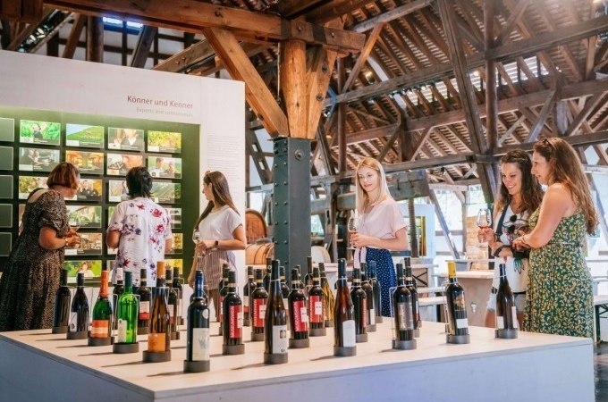 Besucher im Weinbaumuseum betrachten eine Ausstellung mit verschiedenen Weinflaschen. Im Hintergrund sind Informationstafeln und Holzkonstruktionen zu sehen., © Stuttgart Marketing GmbH, Thomas Niedermüller