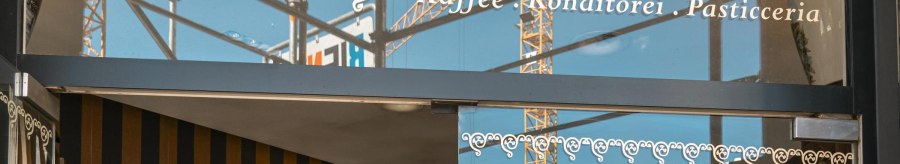 Entrance to the Glora coffee house with decorative lettering on the glass front. Construction cranes can be seen in the background., &copy; SMG, Sarah Schmid