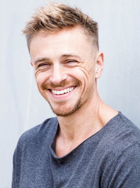 A man with short hair and a beard smiles at the camera. He wears a gray top and stands in front of a gray background., © Rosenau Kultur e.V. A man with short hair and a beard smiles at the camera. He wears a gray top and stands in front of a gray background., © Rosenau Kultur e.V.