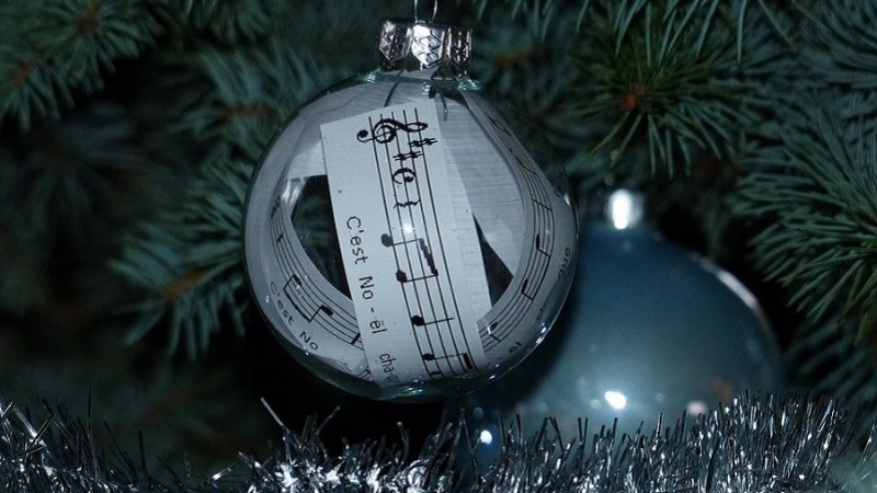Eine Glaskugel mit einem Notenblatt im Inneren hängt an einem Weihnachtsbaum, umgeben von grünen Zweigen und silbernem Lametta., © Pixabay Eine Glaskugel mit einem Notenblatt im Inneren hängt an einem Weihnachtsbaum, umgeben von grünen Zweigen und silbernem Lametta., © Pixabay