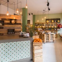 Modern delicatessen with wooden shelves, fresh fruit and vegetables. Hanging lamps and a counter with decorative tiles create a cozy atmosphere., © Benjamin Stollenberg Modern delicatessen with wooden shelves, fresh fruit and vegetables. Hanging lamps and a counter with decorative tiles create a cozy atmosphere., © Benjamin Stollenberg