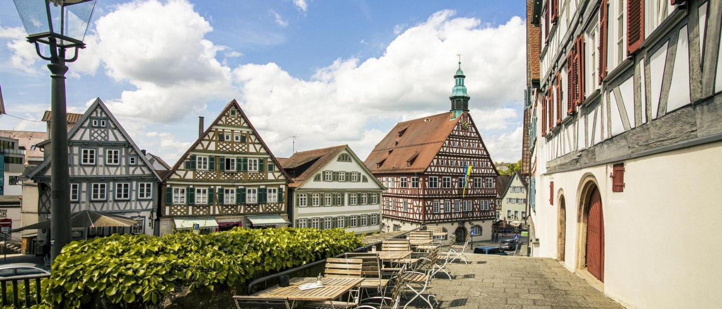 A view of historic half-timbered houses in Backnang. In the foreground are empty seats; in the background is a blue sky with clouds., © SMG Stuttgart Marketing GmbH - Sarah Schmid A view of historic half-timbered houses in Backnang. In the foreground are empty seats; in the background is a blue sky with clouds., © SMG Stuttgart Marketing GmbH - Sarah Schmid