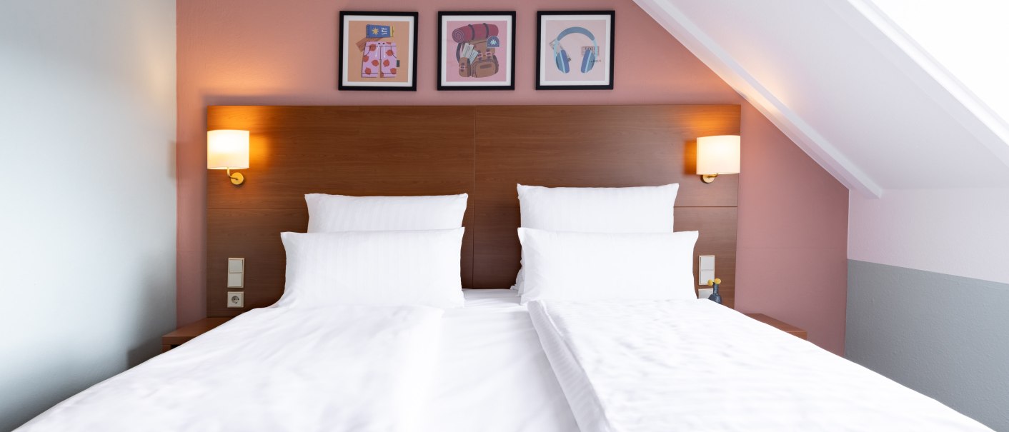 A stylishly furnished hotel room with a large double bed, white sheets, and pillows. Three pictures hang on the wall above the bed., &copy; Novum  Hospitality