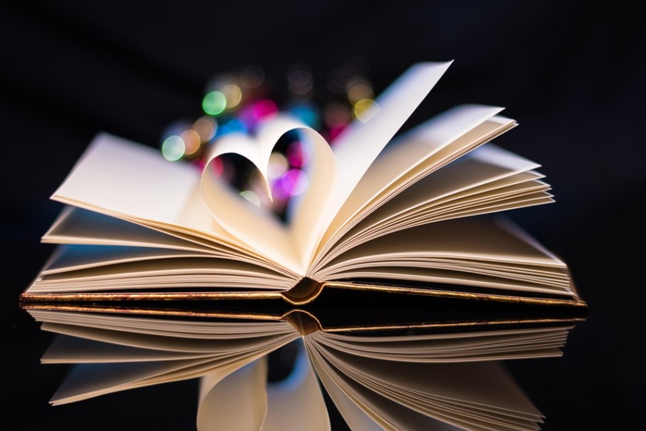 Ein aufgeschlagenes Buch mit einer Herzform aus den Seiten, reflektiert auf einer glänzenden Oberfläche. Im Hintergrund bunte Lichter., © Pixabay Ein aufgeschlagenes Buch mit einer Herzform aus den Seiten, reflektiert auf einer glänzenden Oberfläche. Im Hintergrund bunte Lichter., © Pixabay