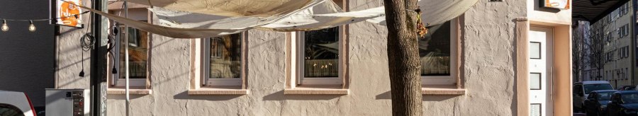 Ein Caf&eacute; mit Sonnensegeln und orangenen St&uuml;hlen im Au&szlig;enbereich. Die Fassade ist beige mit Schriftzug. Ein Baum steht vor dem Eingang., &copy; Stuttgart-Marketing GmbH, Sarah Schmid