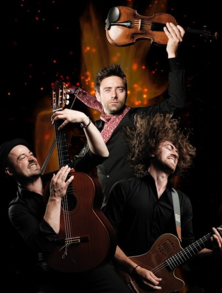 Drei Musiker spielen leidenschaftlich Gitarre und Geige vor einem Hintergrund aus Flammen, was Dynamik und Energie vermittelt., © Theaterhaus Stuttgart e.V. Drei Musiker spielen leidenschaftlich Gitarre und Geige vor einem Hintergrund aus Flammen, was Dynamik und Energie vermittelt., © Theaterhaus Stuttgart e.V.