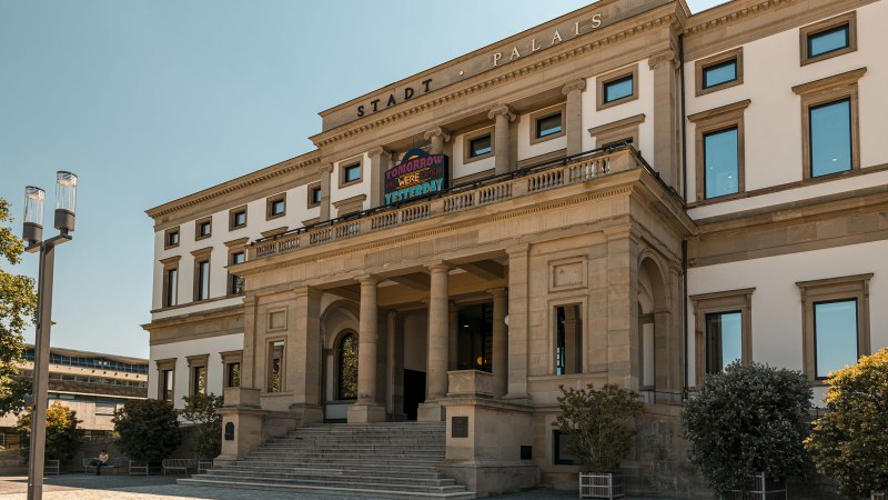 Das StadtPalais mit klassischer Fassade, Säulen und breiter Treppe, unter blauem Himmel. Ein Schild mit bunter Aufschrift ist sichtbar., © Stuttgart Marketing GmbH, Sarah Schmid Das StadtPalais mit klassischer Fassade, Säulen und breiter Treppe, unter blauem Himmel. Ein Schild mit bunter Aufschrift ist sichtbar., © Stuttgart Marketing GmbH, Sarah Schmid