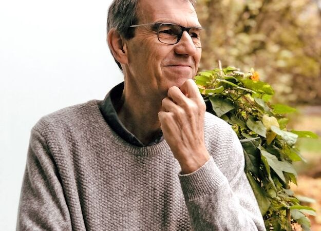 Ein Mann in grauem Pullover steht nachdenklich neben einem Fenster, umgeben von Pflanzen. Er blickt zur Seite und hält seine Hand am Kinn., © Börsenverein des Deutschen Buchhandels, Landesverband Baden-Württemberg e.V.