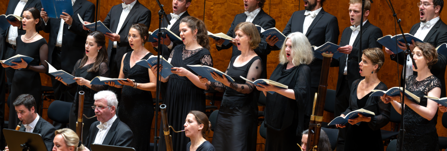 Ein Chor und Orchester in eleganter Kleidung f&uuml;hren ein Werk auf. Die S&auml;nger halten Notenbl&auml;tter und singen mit Ausdruck., &copy; Holger Schneider