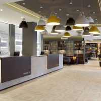 A modern hotel lobby with a front desk, hanging lamps, and a cozy seating area. "Premier Inn" is written on the wall. A lounge is visible in the background., © Premier Inn A modern hotel lobby with a front desk, hanging lamps, and a cozy seating area. "Premier Inn" is written on the wall. A lounge is visible in the background., © Premier Inn