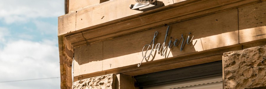 Fassade eines Gebäudes mit dem Schriftzug 'Salieri' und einer Überwachungskamera. Die Sonne wirft Schatten auf die sandfarbene Wand., © SMG, Sarah Schmid Fassade eines Gebäudes mit dem Schriftzug 'Salieri' und einer Überwachungskamera. Die Sonne wirft Schatten auf die sandfarbene Wand., © SMG, Sarah Schmid