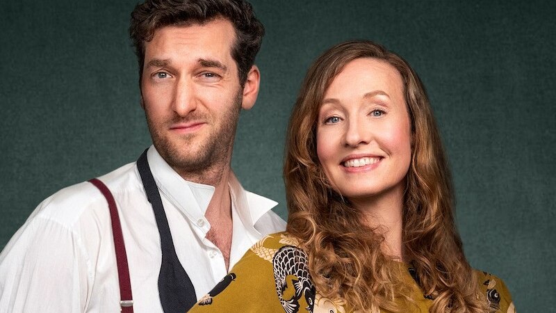 Ein Mann in Hemd und Hosenträgern steht neben einer Frau in einem gemusterten Oberteil. Beide lächeln vor einem neutralen Hintergrund., © Rosenau Kultur e.V. Ein Mann in Hemd und Hosenträgern steht neben einer Frau in einem gemusterten Oberteil. Beide lächeln vor einem neutralen Hintergrund., © Rosenau Kultur e.V.