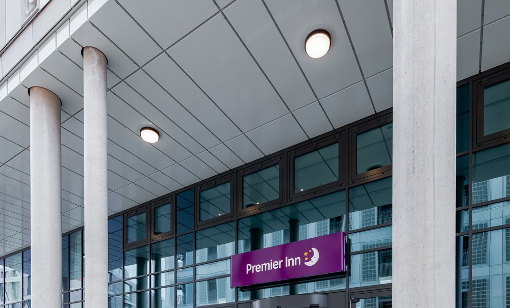 Entrance to a Premier Inn hotel with modern glass façade and large pillars. The logo is visible above the door., © Premier Inn Entrance to a Premier Inn hotel with modern glass façade and large pillars. The logo is visible above the door., © Premier Inn
