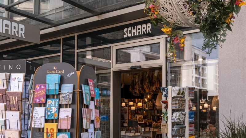 Entrance to the Scharr bookshop with card stands full of greeting cards and hanging flower arrangements. Inside, books and lamps are visible., &copy; SMG Stuttgart Marketing GmbH - Sarah Schmid