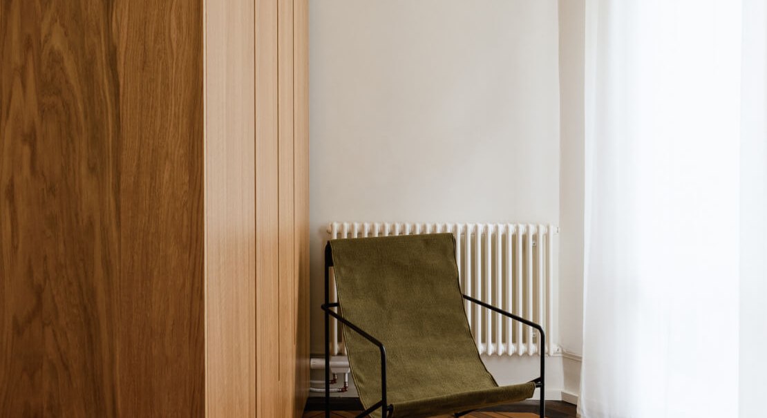 Minimalistischer Raum mit Holzschrank, gr&uuml;nem Stuhl und Parkettboden. Ein Fenster mit wei&szlig;en Vorh&auml;ngen l&auml;sst Licht herein., &copy; Peter Oliver Wolff / DAS EDITH