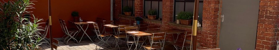 Cozy courtyard with wooden tables and chairs, parasol and plants. Red brick walls and paved floor create an inviting atmosphere., &copy; Gustav Gastro GmbH