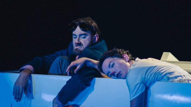 Two people lean over the edge of a white object. One person is wearing safety goggles, the other looks relaxed. Dark background., &copy; FITZ Das Theater animierter Formen
