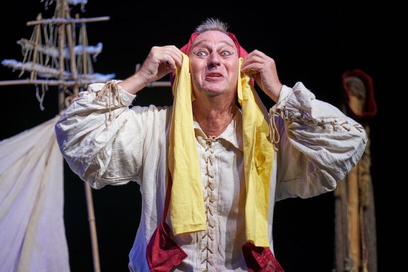 An actor in a historical costume holds a yellow headdress and makes an expressive gesture on stage., © Theaterhaus Stuttgart e.V. An actor in a historical costume holds a yellow headdress and makes an expressive gesture on stage., © Theaterhaus Stuttgart e.V.