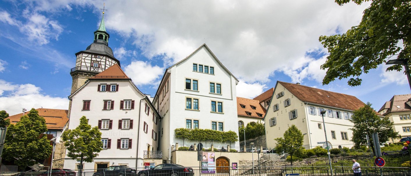 Historic buildings in Backnang, including the Bandhaus and Helferhaus, set against a blue sky with clouds. Trees and street signs in the foreground., © SMG Stuttgart Marketing GmbH - Sarah Schmid Historic buildings in Backnang, including the Bandhaus and Helferhaus, set against a blue sky with clouds. Trees and street signs in the foreground., © SMG Stuttgart Marketing GmbH - Sarah Schmid