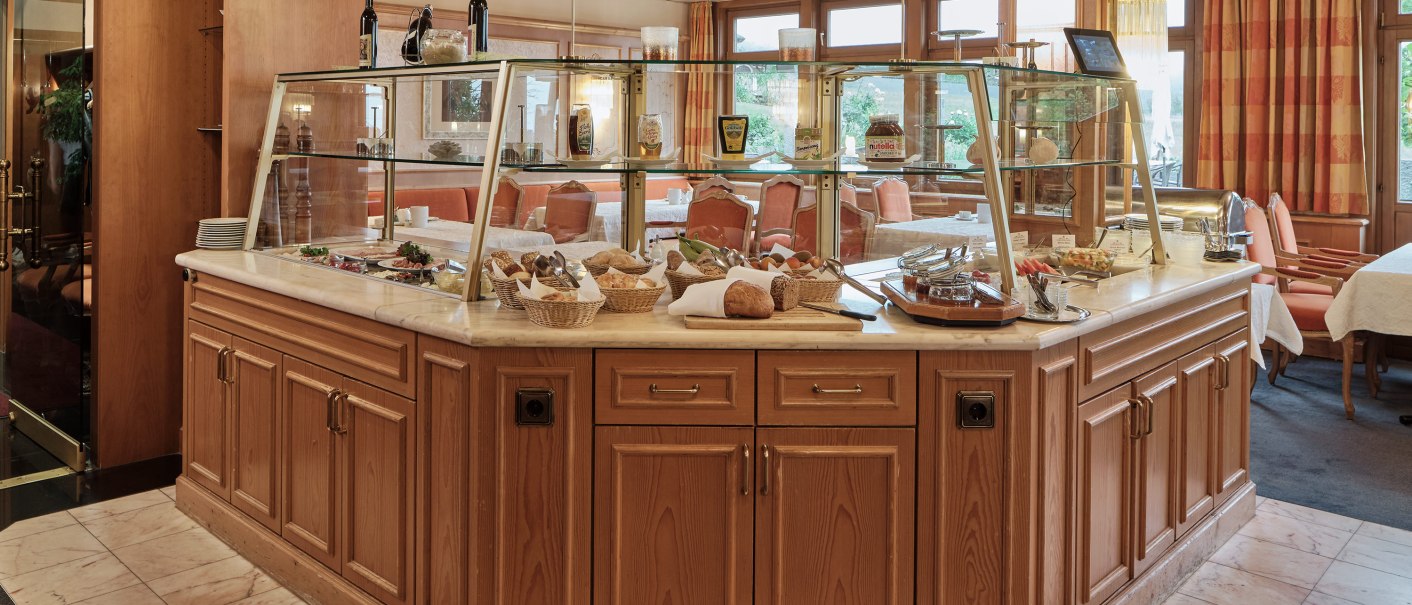 Ein Frühstücksbuffet in einem Hotelrestaurant mit Holzverkleidung und Glasvitrine. Verschiedene Speisen und Getränke sind ausgestellt., © Badhotel Restaurant Stauferland