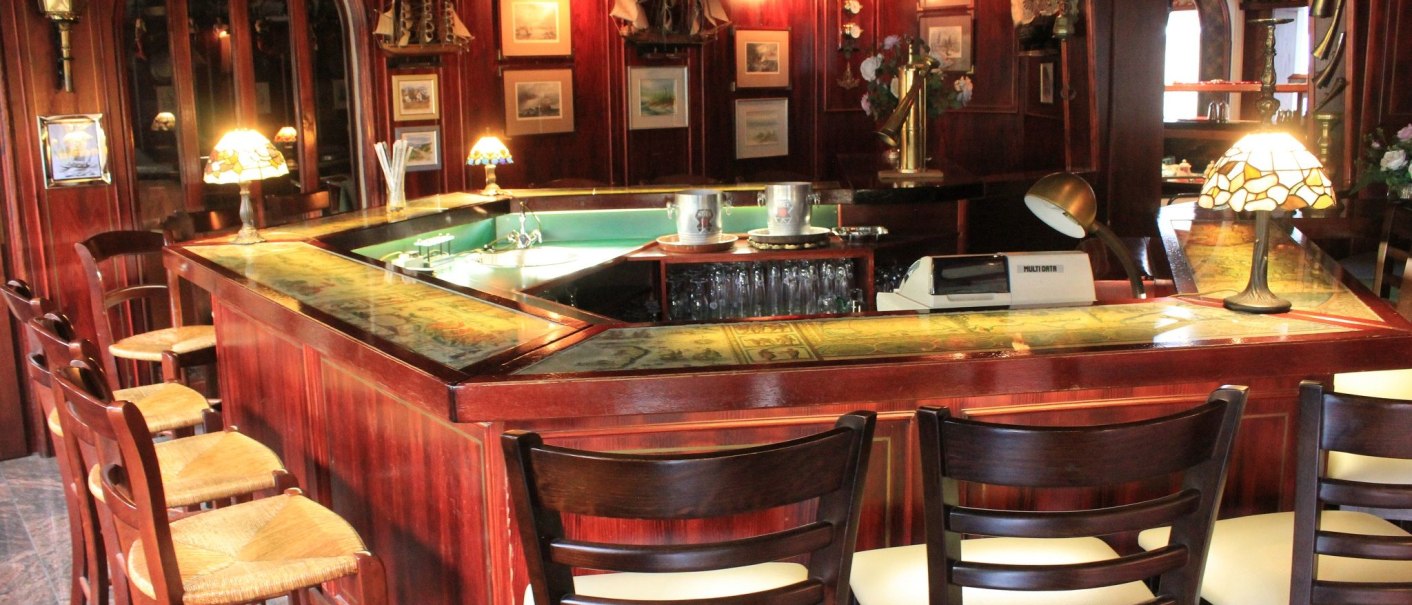 A cozy hotel bar with wooden furniture, bar stools, and decorative lamps. Pictures and nautical decorations hang on the walls., &copy; Hotel Spahr