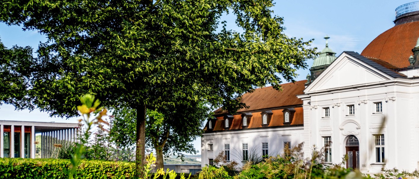 Ein historisches Gebäude mit rotem Dach und weißen Wänden, umgeben von grünen Bäumen und Pflanzen, unter einem klaren blauen Himmel., © DLA Marbach (Anja Bleeser) Ein historisches Gebäude mit rotem Dach und weißen Wänden, umgeben von grünen Bäumen und Pflanzen, unter einem klaren blauen Himmel., © DLA Marbach (Anja Bleeser)