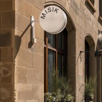 Building with sandstone fa&ccedil;ade, round sign with 'MISIK', windows with plants, closed sunshades on the street., &copy; SMG Stuttgart Marketing GmbH - Sarah Schmid