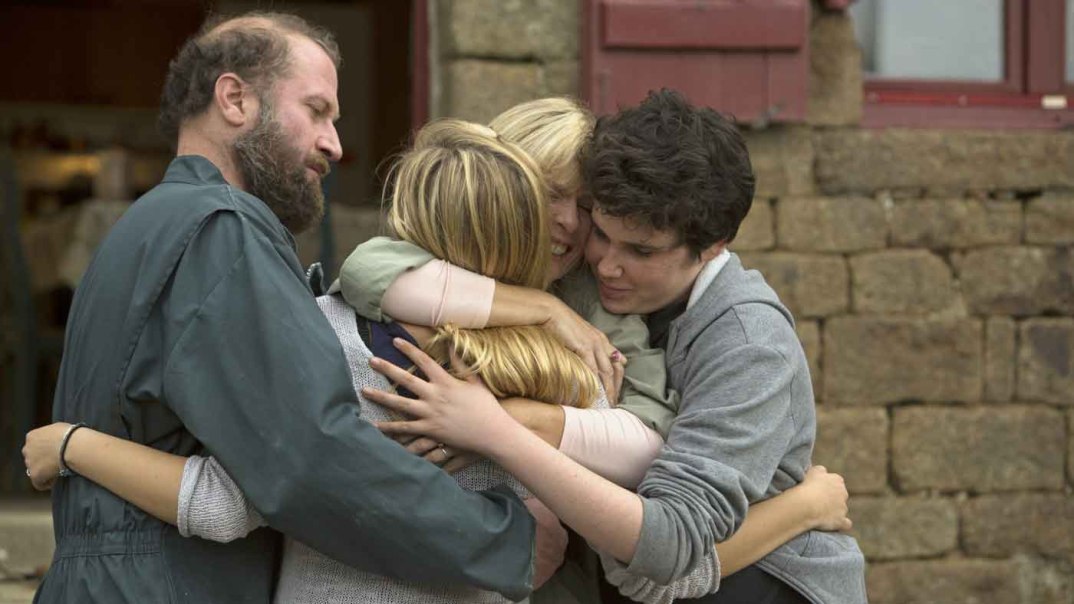 Vier Personen umarmen sich herzlich vor einem steinernen Gebäude. Die Szene strahlt Wärme und Zusammenhalt aus., © Concorde Filmverleih GmbH