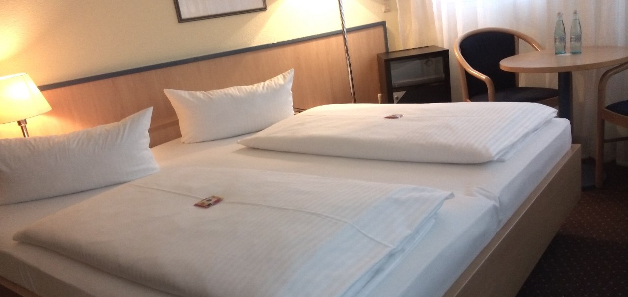 Ein Doppelzimmer mit zwei Betten, Tisch, St&uuml;hlen, Lampen und einem Bild an der Wand. Zwei Wasserflaschen stehen auf dem Tisch., &copy; Central Hotel
