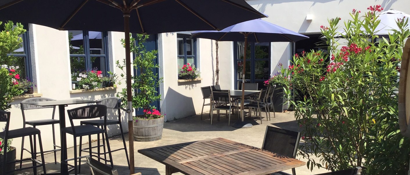 Sonnige Terrasse eines Weinguts mit Holztischen, Stühlen und blauen Sonnenschirmen. Blumen und Pflanzen schmücken den Außenbereich., © Weingut Wöhrwag Sonnige Terrasse eines Weinguts mit Holztischen, Stühlen und blauen Sonnenschirmen. Blumen und Pflanzen schmücken den Außenbereich., © Weingut Wöhrwag
