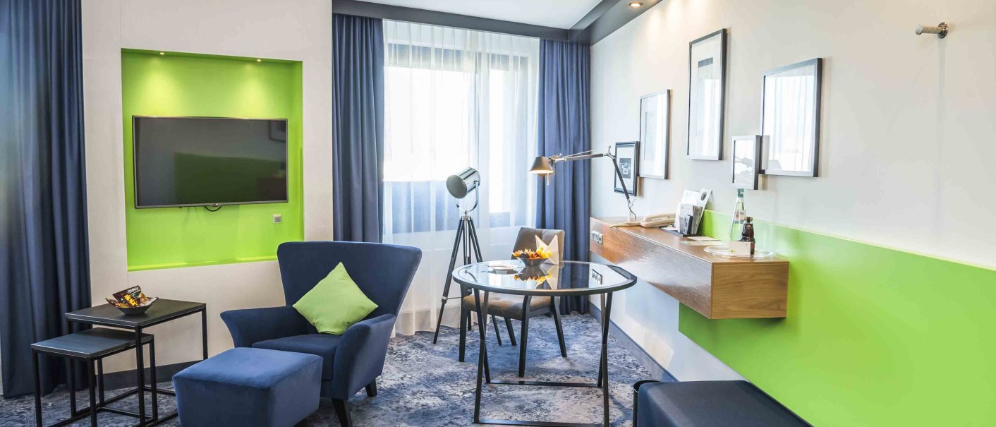 Modern hotel room with blue armchair, green accent, flat screen TV, desk and stylish lighting., &copy; Chandler Photography
