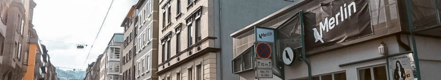 Stra&szlig;enszene in Stuttgart mit dem Kulturzentrum Merlin e.V. rechts im Bild. Die Sonne scheint, Autos parken entlang der Stra&szlig;e., &copy; Merlin, Stuttgart
