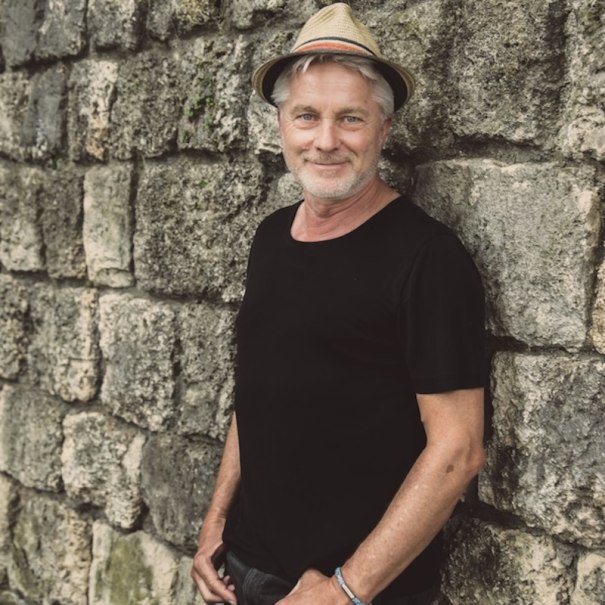 Ein Mann mit Strohhut und schwarzem T-Shirt lehnt lächelnd an einer alten Steinmauer., © Renitenztheater Stuttgart e.V.