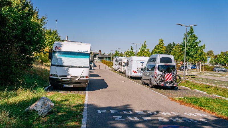 Wohnmobilstellplatz in Fellbach mit geparkten Wohnmobilen und Autos, umgeben von Bäumen und klarem Himmel. Auf der Straße steht 'Feuerwehrzufahrt'., © Stuttgart-Marketing GmbH, Thomas Niedermüller
