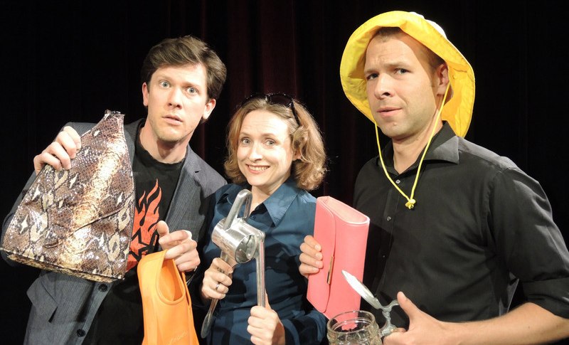 Drei Personen posieren mit verschiedenen Gegenständen: eine Tasche, ein Trichter, eine Zitronenpresse, ein rosa Buch und ein Bierkrug. Hintergrund ist dunkel., © Theaterhaus Stuttgart e.V.