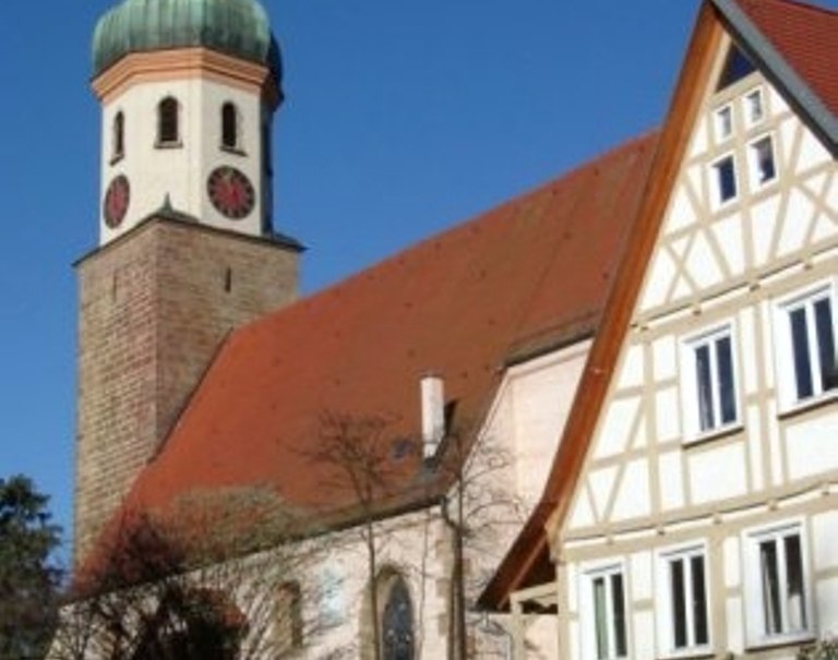 Die Ulrichskirche mit ihrem markanten Turm und einem angrenzenden Fachwerkhaus vor blauem Himmel., © TOMAS