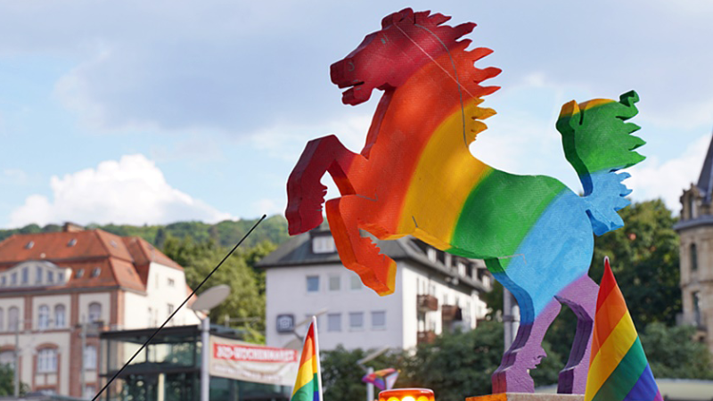 Ein Regenbogen-Pferd aus Pappe vor historischen Gebäuden und blauem Himmel bei der Stuttgart PRIDE., © IG CSD Stuttgart e.V. Ein Regenbogen-Pferd aus Pappe vor historischen Gebäuden und blauem Himmel bei der Stuttgart PRIDE., © IG CSD Stuttgart e.V.