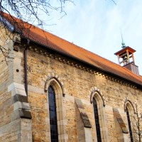 Steinkirche mit rotem Satteldach, Rundfenster und kleinem Glockenturm, von kahlen Ästen und Herbstbäumen umrahmt., © St. Katharina Stuttgart Steinkirche mit rotem Satteldach, Rundfenster und kleinem Glockenturm, von kahlen Ästen und Herbstbäumen umrahmt., © St. Katharina Stuttgart
