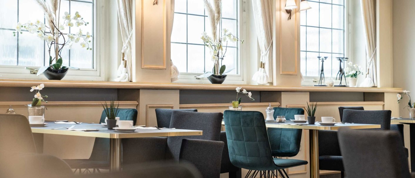 An elegant breakfast room with set tables, modern chairs, and large windows. Subtle decor featuring plants and stylish lamps., &copy; Flairhotel Vier Jahreszeiten