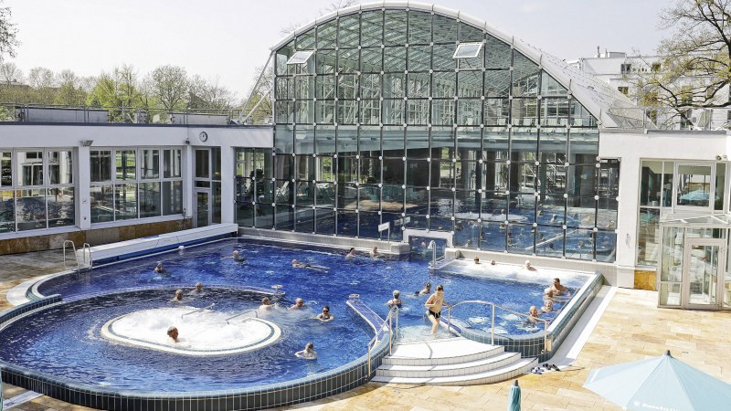 Das SoleBad Bad Cannstatt zeigt ein modernes Schwimmbecken mit Glasfassade. Menschen entspannen im Wasser und auf Liegestühlen., © Stuttgarter Bäder