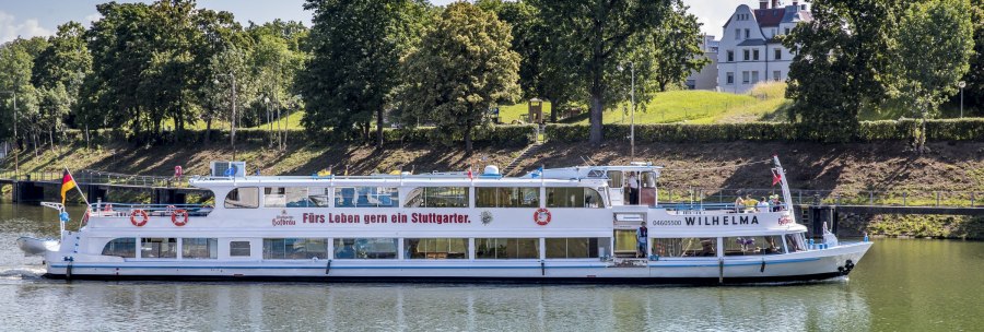 The passenger ship MS Wilhelma sails on a river, surrounded by trees and a building in the background. Inscription: "A Stuttgart resident for life.", © all copyrights are reserved by maks richter