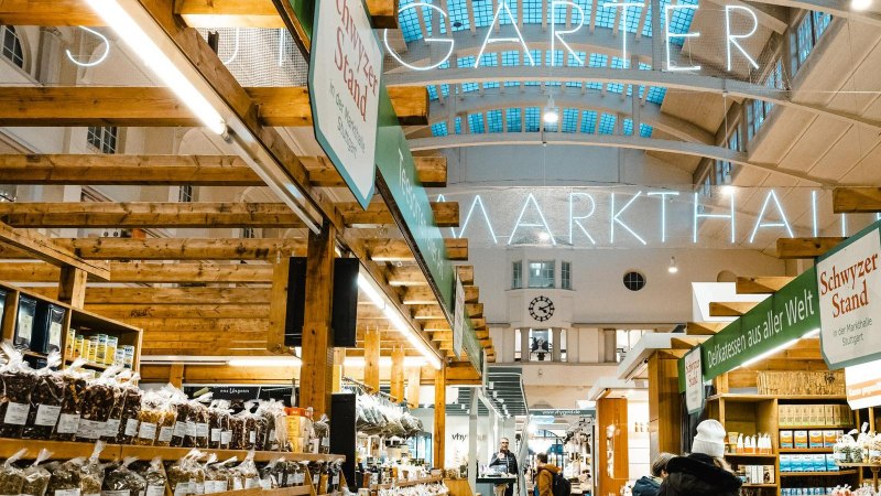 Innenansicht der Stuttgarter Markthalle mit Holzständen, Leuchtschrift und verschiedenen Verkaufsständen für Delikatessen., © Stuttgart-Marketing GmbH, Sarah Schmid