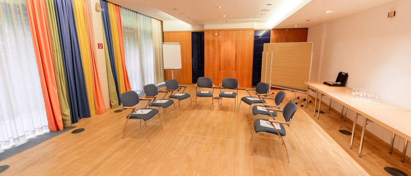 A meeting room with chairs in a circle, flipchart, colorful curtains and a table with glasses., © PLAZA Hotelgroup GmbH