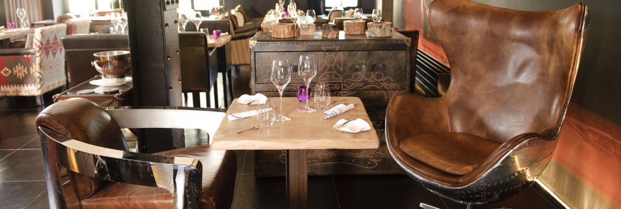 A stylishly furnished restaurant with leather armchairs and a laid table. More tables and chairs can be seen in the background., © none