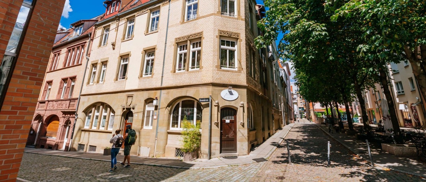 Historische Gebäude im Bohnenviertel mit Kopfsteinpflasterstraße und Bäumen. Zwei Personen spazieren entlang der Brennerstraße., © Thmoas Niedermüller