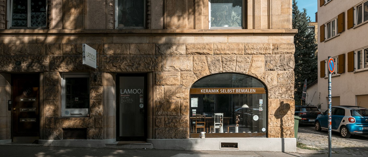 Fassade eines Gebäudes mit Schaufenster, das 'Keramik selbst bemalen' zeigt. Links ein Schild mit 'LAMOOI'. Autos und Bäume im Hintergrund., © SMG, Sarah Schmid