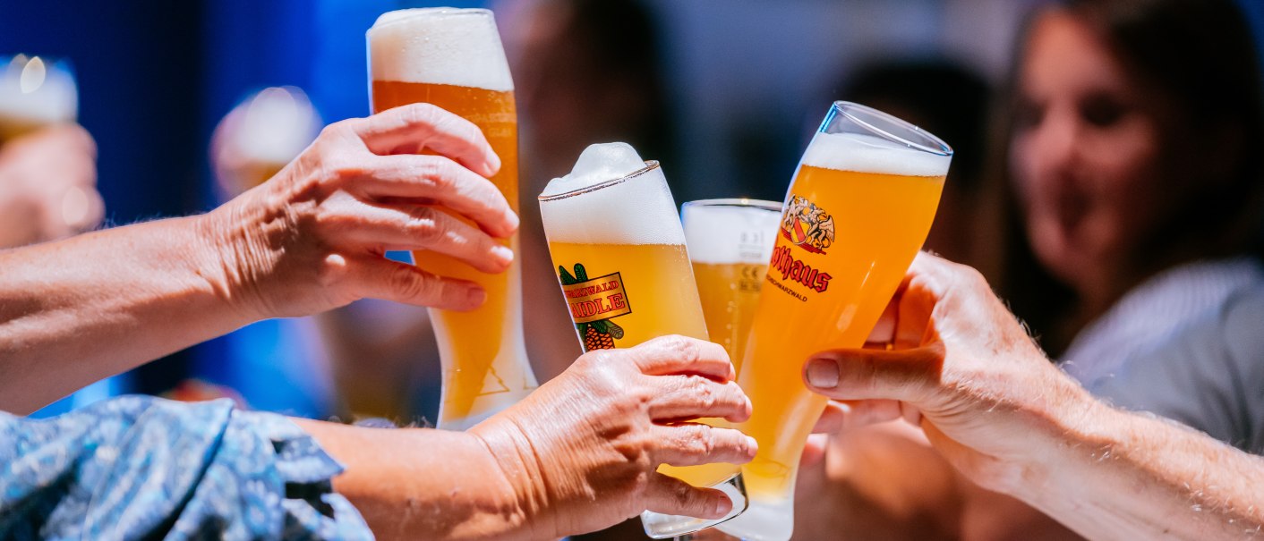 Mehrere Personen stoßen mit gefüllten Biergläsern an, im Hintergrund sind unscharf weitere Personen zu sehen., © Stuttgart-Marketing GmbH, Thomas Niedermüller