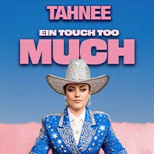 A person in a glittering cowboy outfit stands in front of a blue sky. The lettering "TAHNEE - EIN TOUCH TOO MUCH" can be seen above it in pink., &copy; links im Bild